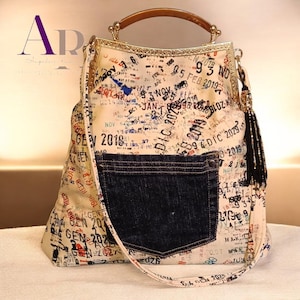 May include: A cream-colored handbag featuring a repeating pattern of black, blue, and red travel-style date stamps. The bag has a dark blue denim pocket on the front, a gold-toned metal frame, a brown handle, and a black beaded tassel on the side.