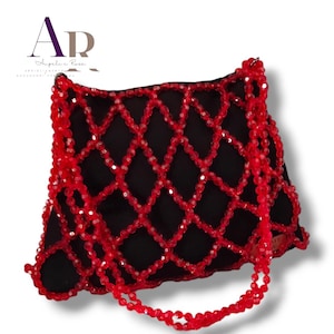 May include: Black handbag with a red beaded overlay in a diamond pattern. The bag has a matching red beaded strap and trim. The brand name "Angelie Rose" is visible in the upper left corner.