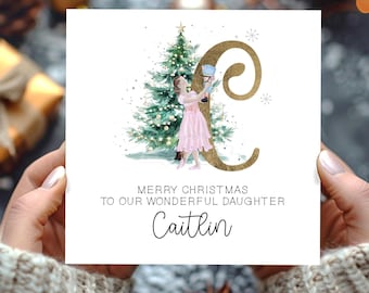 Puede incluir: Una tarjeta de Navidad con una ilustración en acuarela. La tarjeta presenta una bailarina con un vestido rosa, un árbol de Navidad y la letra "C" dorada. El texto dice "Merry Christmas to our wonderful daughter Caitlin".