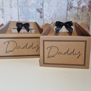 May include: Two brown cardboard gift boxes with black ribbon bows and the word "Daddy" printed on the front.