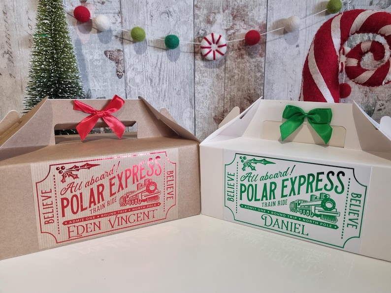 May include: Two gift boxes with handles, one brown and one white. The brown box has a red bow and a label that reads "Polar Express" with the name "Eden Vincent." The white box has a green bow and the name "Daniel."