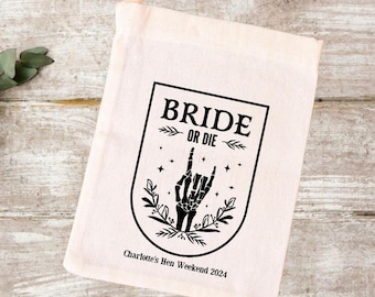 May include: A white cotton tote bag with a black graphic design. The graphic features a skeleton hand making a rock and roll sign with the text "Bride or Die" in a black banner above the hand. The text "Charlotte's Hen Weekend 2024" is printed below the graphic.