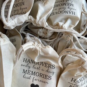 May include: A pile of white cotton drawstring bags with black text that reads "Hangovers only last a day Memories last forever".