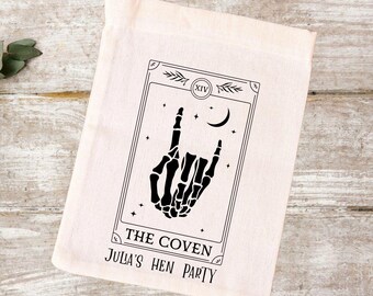 May include: A white cotton tote bag with a black and white tarot card design. The card features a skeleton hand making a rock and roll hand gesture. The text on the card reads "The Coven" and "Julia's Hen Party".