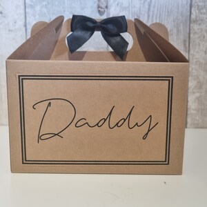 May include: A brown cardboard gift box with a black ribbon and the word "Daddy" printed on the front.