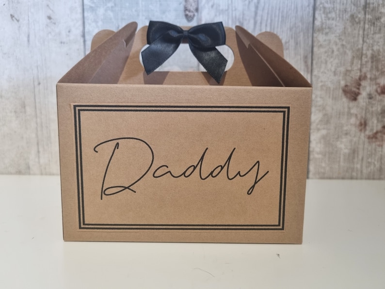 May include: A brown cardboard gift box with a black ribbon and the word "Daddy" printed on the front.