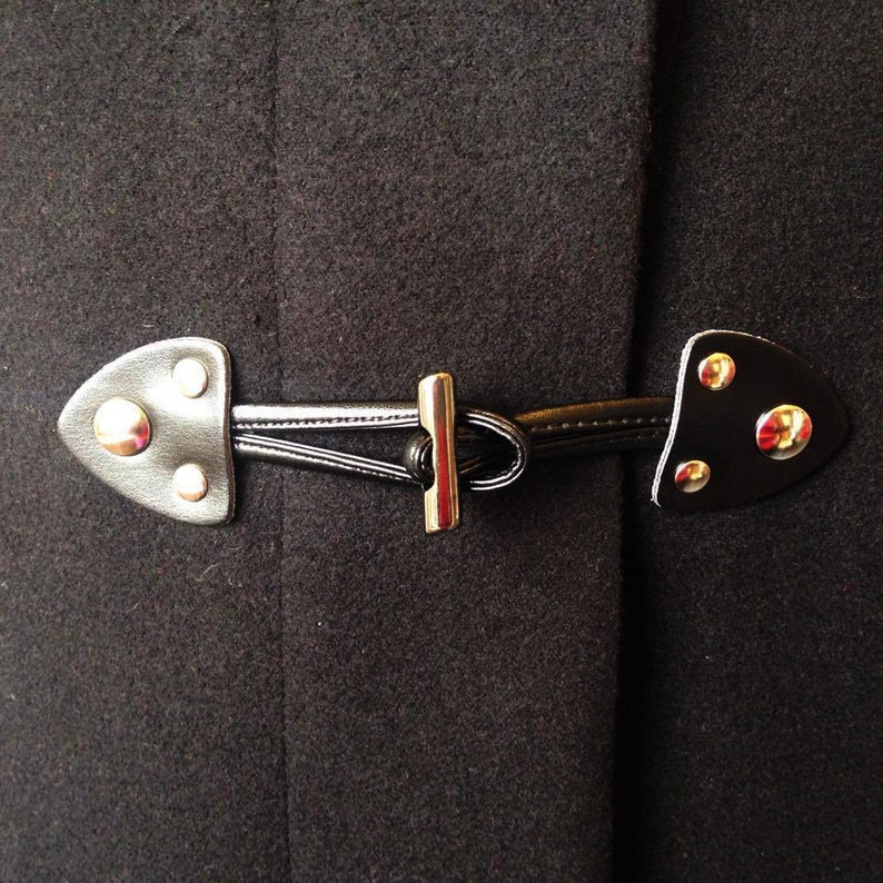 May include: A black wool coat with a silver metal toggle closure. The toggle is made of two pieces of leather with metal accents.