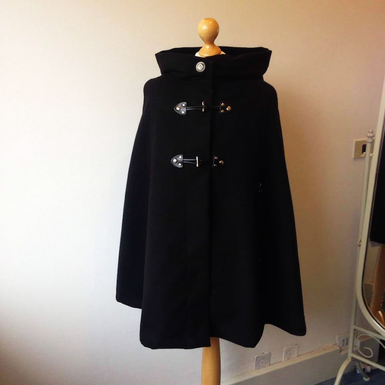 May include: A black hooded cape with a high collar and two sets of black buckles. The cape is made of a thick, warm fabric and has a simple, elegant design.
