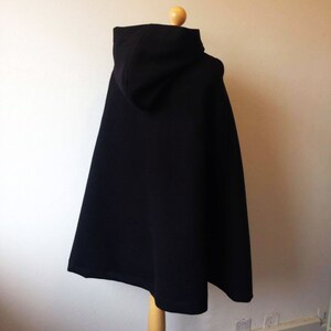 May include: A black hooded cape with a simple design. The cape is made of a soft, smooth fabric and has a relaxed fit.