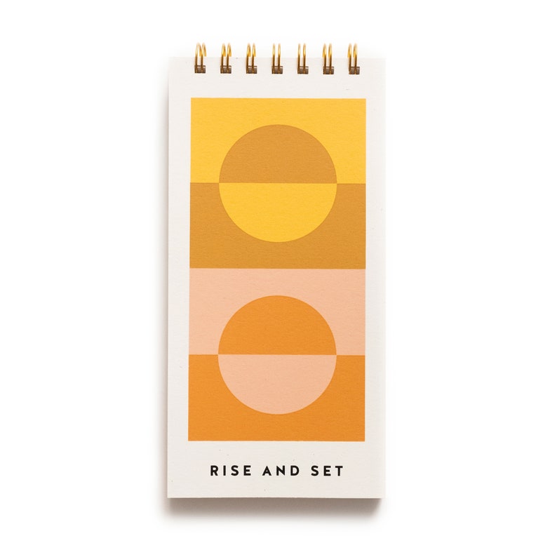 May include: A white notepad with a gold spiral binding. The cover features a geometric design with two orange and yellow circles, a pink and orange circle, and the text "RISE AND SET".