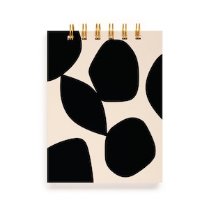May include: A spiral-bound notepad with a cream-colored cover featuring a pattern of large, irregular black shapes. The spiral binding is gold-colored.