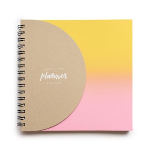 May include: A spiral-bound planner with a half-circle cover. The cover is tan with the word "planner" in cursive. The pages have a gradient of yellow to pink. The planner is designed for month, week, and open dates.