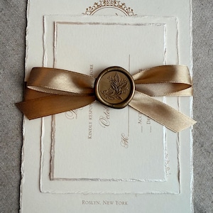 May include: Elegant wedding invitation suite with layered ivory paper, a gold ribbon, and a wax seal. The invitation includes the text "Kindly Respond" and "Roslyn, New York". The suite is tied with a gold satin ribbon.