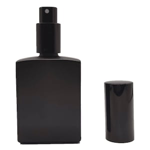 K&ouml;nnte beinhalten: Eine rechteckige Parf&uuml;mflasche aus mattem schwarzem Glas mit einem schwarzen Spr&uuml;hmechanismus und einer separaten zylindrischen schwarzen Kappe, die rechts daneben steht. Die Flasche hat eine glatte, undurchsichtige Oberfl&auml;che und einen Spr&uuml;hkopf.