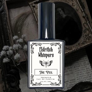 K&ouml;nnte beinhalten: Ein rechteckiger Glasparf&uuml;mflakon mit dunklem Verschluss und wei&szlig;em Etikett. Das Etikett zeigt den Text Eldritch Whispers, eine Mottenillustration und den Text The Veil, Premium Eau de Parfum, Fill Wt. 30ml, umrahmt von schwarzem Dekor.