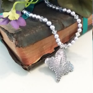 Ras de cou gris argenté doux avec pendentif.  Doux détail de perles et de cristaux avec pendentif fleur de lys en argent vieilli.