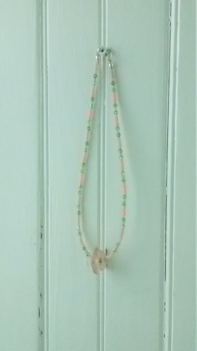 A pale pink quartz flower serves as the pendant. Light pink seed beads with green crystals Sweet pink and green choker