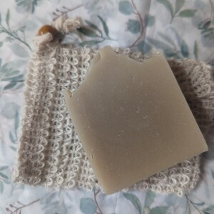 May include: A beige bar of soap in a white crocheted soap bag with a wooden button.