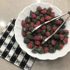 May include: A white bowl filled with red and black berries. The berries are arranged in a random pattern and are surrounded by a silver serving utensil.