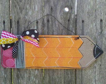 May include: A wooden pencil-shaped door hanger painted in orange, gray, and black with a pink, yellow, and black polka dot bow.