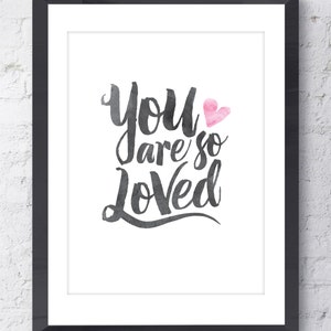 May include: A black and white watercolor print with the text "You are so Loved" in a cursive font. A pink watercolor heart is above the word "Loved".
