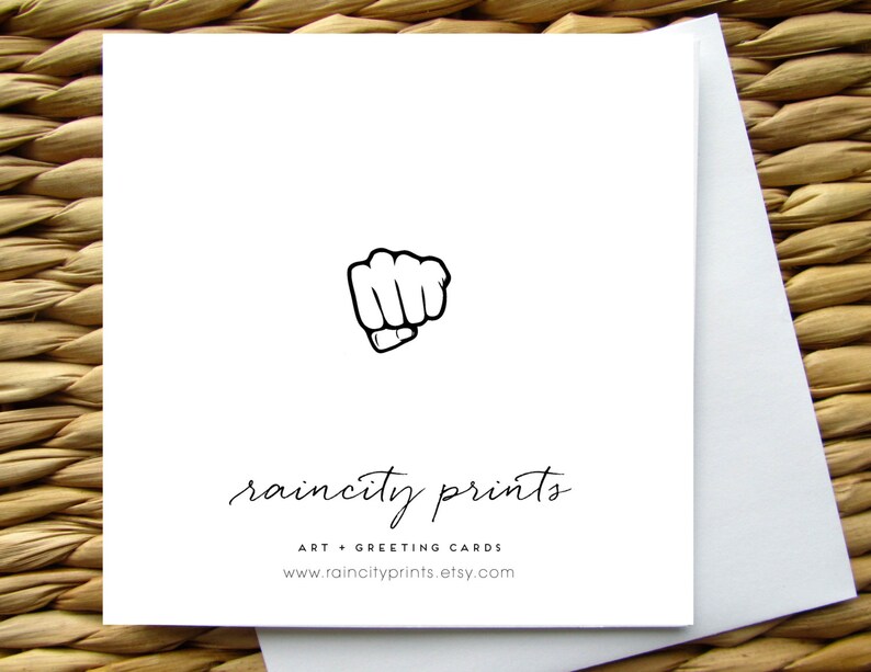 Puede incluir: Una tarjeta de felicitaci&oacute;n blanca con una ilustraci&oacute;n de pu&ntilde;o negro y el texto "raincity prints" en fuente cursiva negra. Debajo del texto se encuentra "ART + GREETING CARDS" y la direcci&oacute;n del sitio web "www.raincityprints.etsy.com".