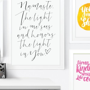 May include: White framed art prints with inspirational quotes. One print reads "Namaste. The light in me sees and honors the light in You!" in black script. Other prints feature colorful watercolor backgrounds with uplifting phrases.
