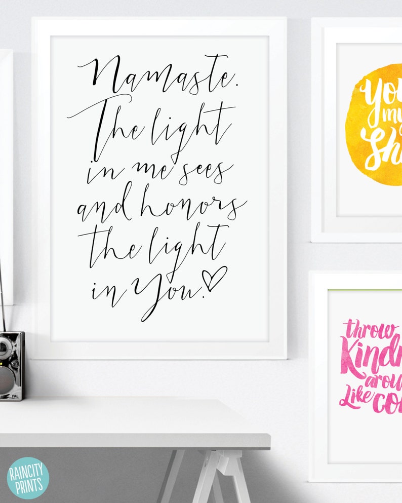 May include: White framed art prints with inspirational quotes. One print reads "Namaste. The light in me sees and honors the light in You!" in black script. Other prints feature colorful watercolor backgrounds with uplifting phrases.