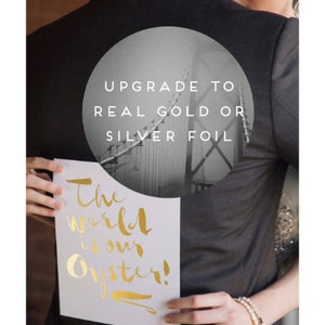 May include: A couple holding a white card with gold lettering that says "The world is our oyster!" The man is wearing a gray suit jacket with a circle on the back that says "Upgrade to real gold or silver foil".