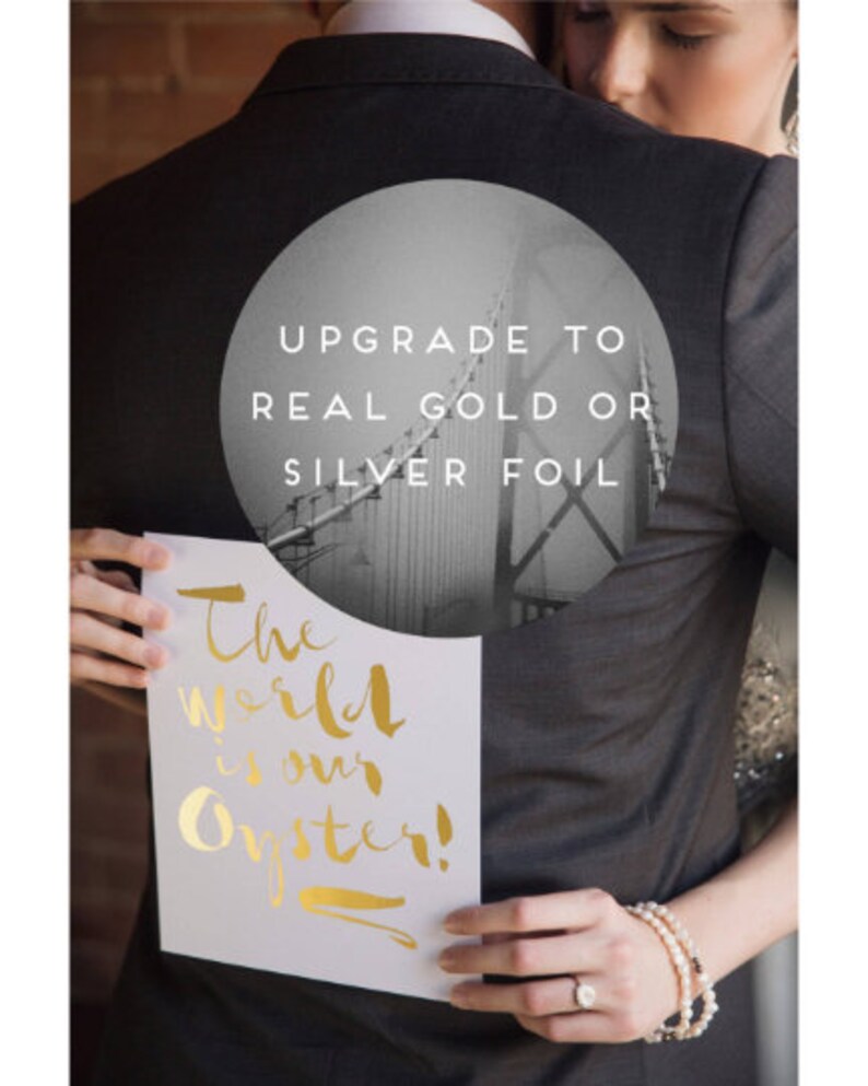 May include: A couple holding a white card with gold lettering that says "The world is our oyster!" The man is wearing a gray suit jacket with a circle on the back that says "Upgrade to real gold or silver foil".