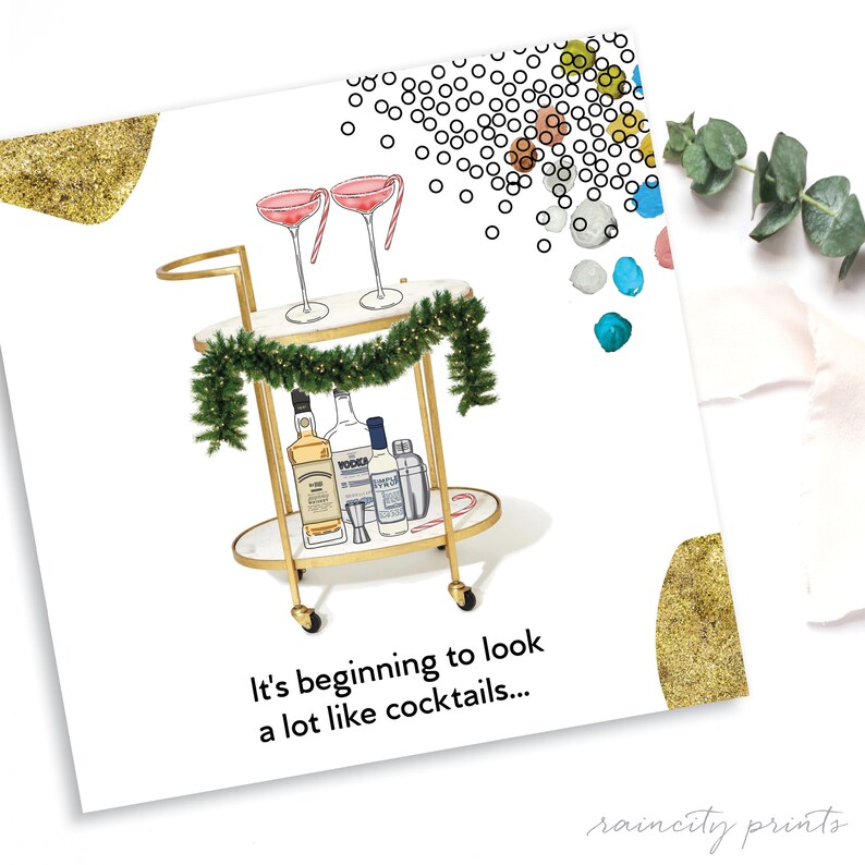 May include: A gold bar cart with a garland of greenery, two pink cocktails, a bottle of vodka, a bottle of whiskey, a bottle of gin, a cocktail shaker, and a candy cane. The text "It's beginning to look a lot like cocktails..." is below the cart.