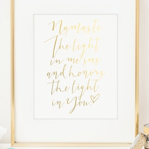 May include: A framed print with gold lettering on a white background. The text reads "Namaste. The light in me sees and honors the light in You!" The frame is gold, and the print is displayed on a white surface.