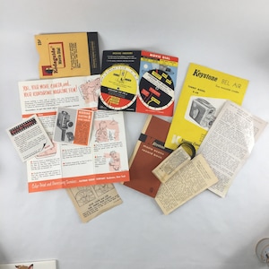 May include: A collection of vintage camera and film instructions and guides. The guides are printed on paper and feature black and white illustrations of cameras and film. The text includes the words "Kodaguide Movie Dial", "Keystone Bel Air", "Turret Model K-48", and "Movie Scene Record Book".