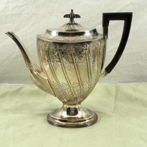 May include: A silver teapot with an ornate design and a black handle. The teapot has a round body and a pedestal base.