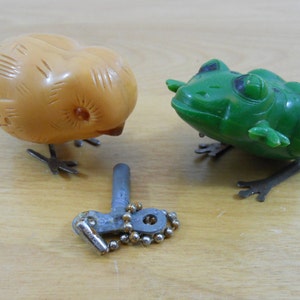 以下が含まれることがあります： 黄色の鳥と緑色のカエルの2つのヴィンテージのゼンマイ仕掛けのおもちゃのセット。シルバーのゼンマイキー付きです。