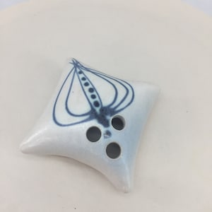 May include: A white ceramic flower vase with a blue and white abstract design. The vase has three holes in the bottom for holding flowers.