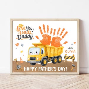 Puede incluir: Impresión enmarcada con una ilustración de camión volquete amarillo y huellas de manos naranjas. El texto dice "Love you Loads, Daddy" y "Happy Father's Day!" con el nombre "Olivia". La obra tiene un tema de construcción.