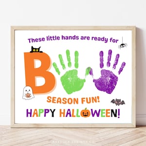 Puede incluir: Un cartel enmarcado con temática de Halloween con la palabra "BOO" formada por una letra naranja y huellas de manos verdes. También se incluyen huellas de manos moradas, un fantasma, un gato negro, una araña y un murciélago. El texto dice "SEASON FUN! HAPPY HALLOWEEN!"