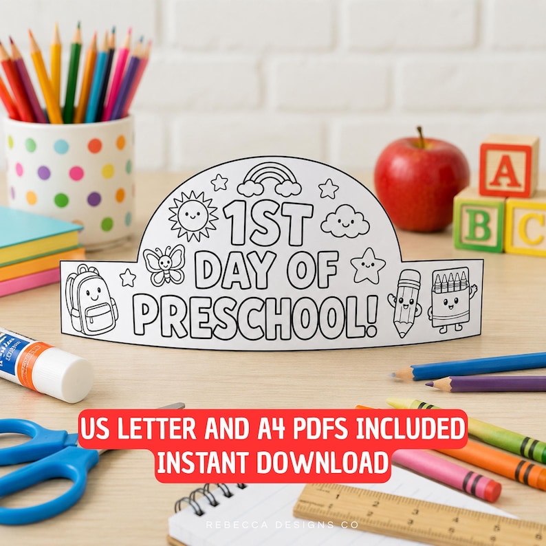 Op de afbeelding: Een witte papieren kroon met zwarte lijntekeningen met de tekst 1ST DAY OF PRESCHOOL!, omringd door illustraties van een zon, regenboog, wolken, sterren, een vlinder, een rugzak, een potlood en een doosje kleurpotloden voor activiteiten.