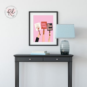 May include: A framed print with a pink background and three hands holding signs that read "You Go Girl", "Girl Pwr", and "The Future Is Female".