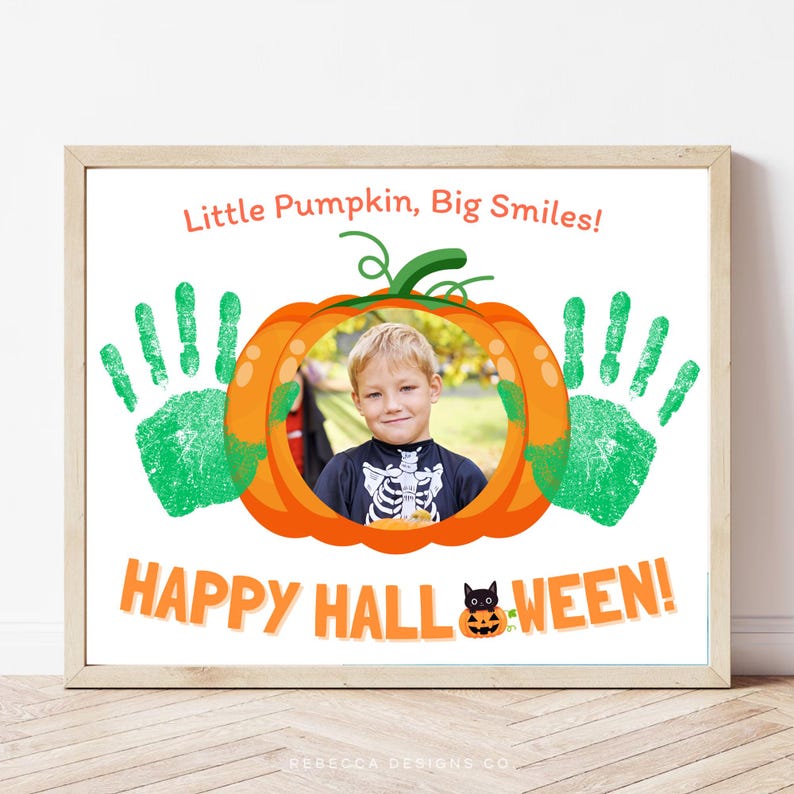 May include: A rectangular print in a light wood frame featuring a central orange pumpkin graphic with a circular photo cutout of a child. The design includes two green handprints, the text Little Pumpkin, Big Smiles!, and HAPPY HALL-WEEN!