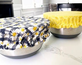 May include: Two stainless steel mixing bowls with fabric covers. One bowl has a yellow and white honeycomb pattern cover, the other has a black and white gingham pattern with white daisies.