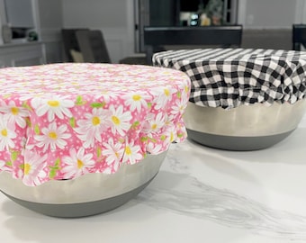 May include: Two stainless steel mixing bowls with fabric covers. One bowl has a pink and white floral print cover, and the other has a black and white checkered cover.