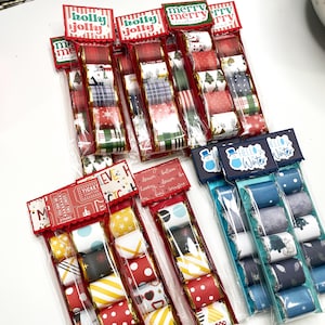 Peut inclure: Plusieurs sacs en cellophane remplis de rubans décoratifs. Chaque sac est orné d'une étiquette décorative avec des textes comme "Holly Jolly" ou "Hello Winter". Les rubans présentent divers motifs, notamment des pois, des rayures et des motifs de vacances. Vue de dessus.