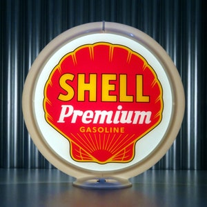 May include: A white round gas station sign with a red and yellow shell logo. The text on the sign reads "SHELL Premium GASOLINE".