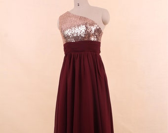 May include: A long, burgundy chiffon dress with a one-shoulder neckline. The top of the dress is adorned with gold sequins.