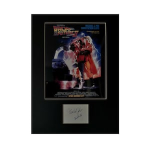 May include: A framed movie poster for Back to the Future Part II featuring Michael J. Fox and Christopher Lloyd. The poster is signed by both actors. The poster is set against a black background.