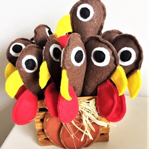 May include: A brown felt turkey centerpiece with red and yellow felt accents. The turkey is sitting in a brown basket with straw and a pumpkin-shaped base.