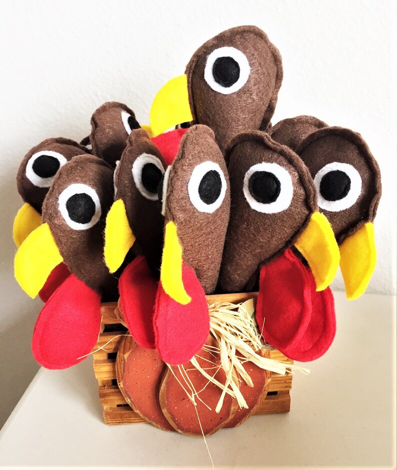 May include: A brown felt turkey centerpiece with red and yellow felt accents. The turkey is sitting in a brown basket with straw and a pumpkin-shaped base.