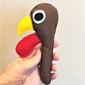 May include: A brown felt turkey puppet with a red wattle, yellow beak, and black eye.